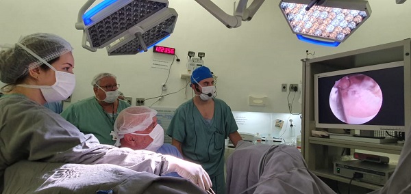 #PraCegoVer: Na Imagem, médicos vestidos com aventais verde, azul e cinza, realizando ultrassom em paciente.